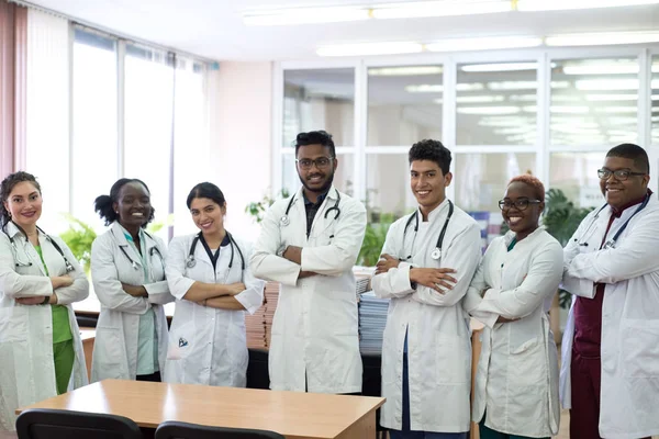 Een groep artsen in de ziekenhuisgang. Team van gemengde ras jonge mannen in witte jassen, met fonendoscopen, glimlachend — Stockfoto