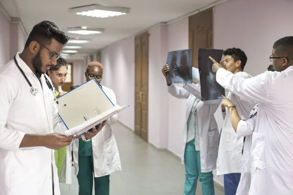 Un equipo de médicos jóvenes. Un grupo de personas de diferentes razas, de diferentes sexos, vestidas con ropa médica, en el pasillo del hospital, mirando una radiografía, discutiendo sobre medicina — Foto de Stock