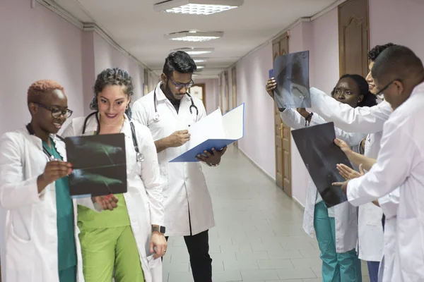 Команда молодых врачей. Группа людей разных рас, разных полов, одетых в медицинскую одежду, в коридоре больницы, смотрит на рентген, обсуждая медицину — стоковое фото