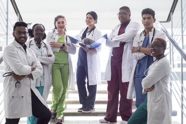 Gemengd ras, een groep jonge dokters, studenten. Mannen en vrouwen in witte jassen, met fonendoscopen, glimlachend, poserend op de treden van de ziekenhuisgang — Stockfoto