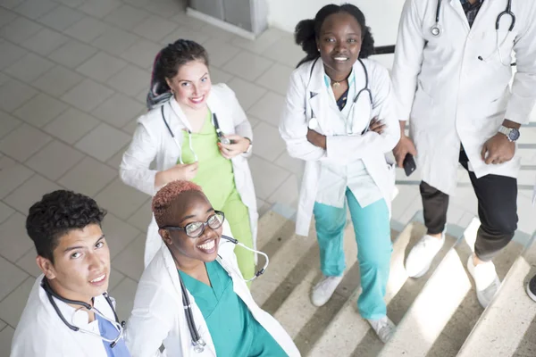 Los médicos están sentados en las escaleras del hospital. Un grupo de jóvenes de diferente género, de raza mixta, en ropas médicas, con fonendoscopios. Usa smartphone, estudia historias médicas, estudia rayos X — Foto de Stock