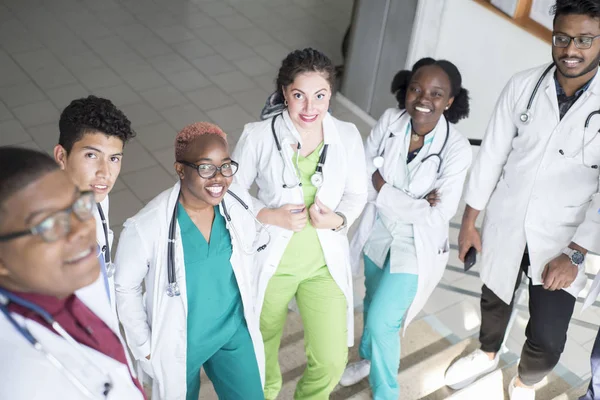 Artsen zitten op de trappen van het ziekenhuis. Een groep jongeren van verschillend geslacht, gemengd ras, in medische kleding, met fonendoscopen. smartphone gebruiken, medische dossiers bestuderen, röntgenfoto 's bestuderen — Stockfoto