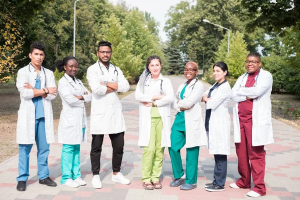 Lag av blandras läkare. Grupp av unga människor av olika kön i färgade medicinska kläder, står på gatan, på gatan, med fonoskop, poserar, ler — Stockfoto