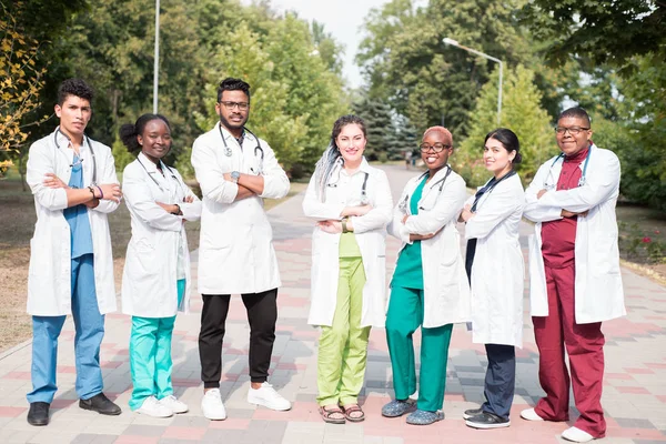 Equipo de médicos de raza mixta. Grupo de jóvenes de diferente género en ropas médicas de color, de pie en la calle, en la calle, con fonendoscopios, posando, sonriendo —  Fotos de Stock