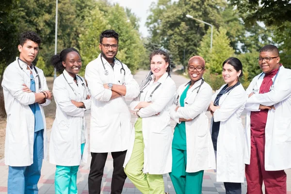 Команда лікарів змішаної раси. Група молодих людей різної статі в кольоровому медичному одязі, що стоїть на вулиці, на вулиці, з фонендоскопами, позує, посміхається — стокове фото