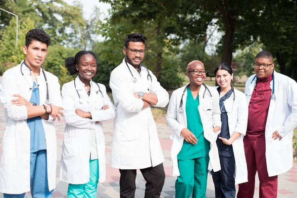 Equipo de médicos de raza mixta. Grupo de jóvenes de diferente género en ropas médicas de color, de pie en la calle, en la calle, con fonendoscopios, posando, sonriendo — Foto de Stock