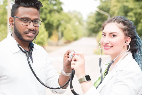 a pair of doctors. Young people: Indian guy and white girl. In medical coats, smiling, they put phonendoscopes to each other, symbolizing the friendship of peoples, doctors
