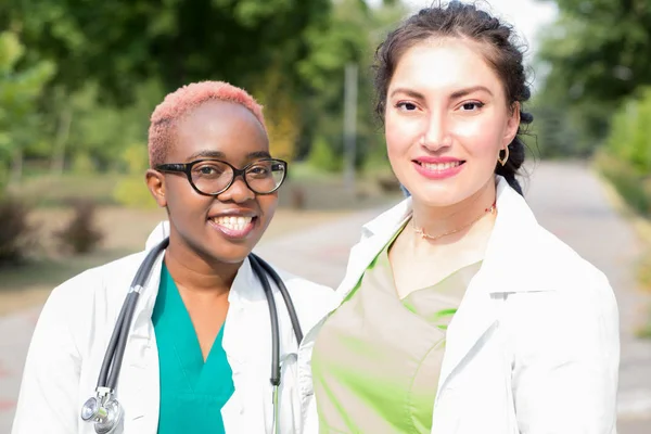 Пара молодих лікарів. Студенти-медики сміються над білими халатами та стетоскопом. На відкритому повітрі — стокове фото