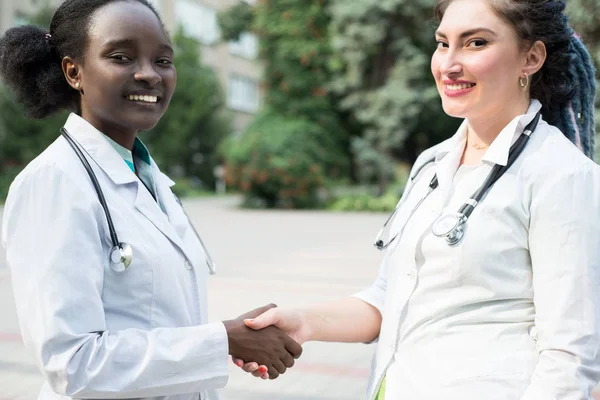 Bir çift doktor. İki güzel kız, Afrikalı ve Avrupalı, beyaz önlüklü, fonendoskoplu, sokakta tokalaşan