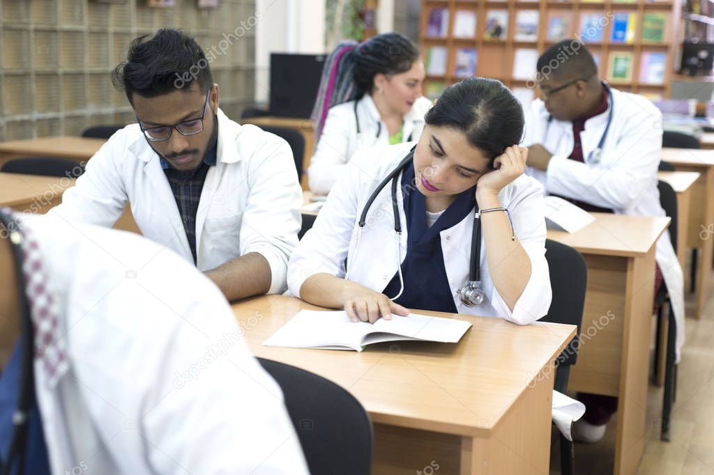 a group of young multiethnic races, medical students. Read textbooks while sitting at a desk. Dullness of exams, study