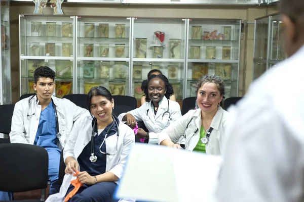 medical teacher, conducts a lesson for medical students. A group of young people of different gender, mixed races, sit on chairs in the classroom