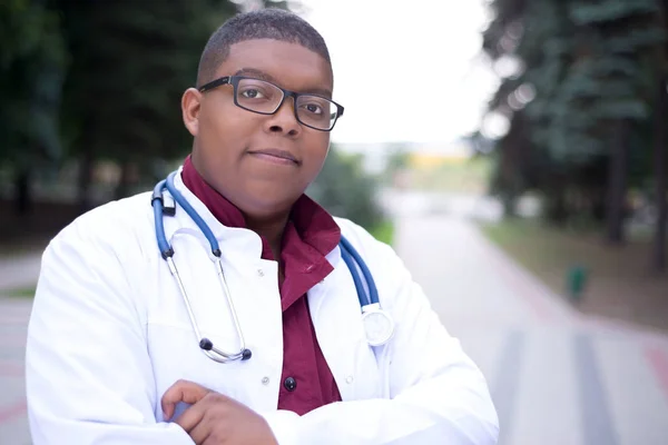 Портрет афроамериканського лікаря. Молодий хлопець, в медичному одязі, в окулярах, з фонендоскопом. На відкритому повітрі — стокове фото