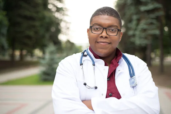 Портрет афроамериканського лікаря. Молодий хлопець в медичному одязі, одягнений в окуляри, посміхається. На відкритому повітрі — стокове фото