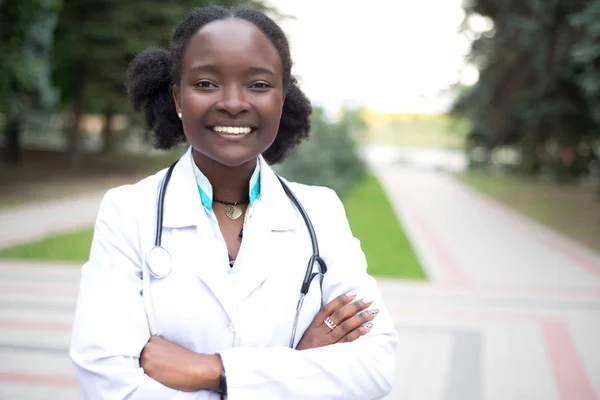 Ritratto di una ragazza afroamericana. Medico in camice bianco, con fonendoscopio, sorriso, all'aperto — Foto Stock