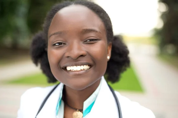 Ritratto di una ragazza afroamericana. Medico in camice bianco, con fonendoscopio, sorriso, all'aperto — Foto Stock