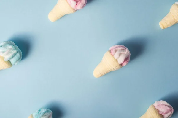 Cukierki piankowe, w postaci małych rożków lodowych w kolorze niebieskim i różowym, na niebieskim tle. Pastelowe odcienie. Minimalna koncepcja lata — Zdjęcie stockowe
