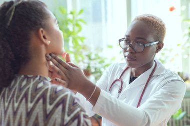 Afrikalı kadın doktor boğazı ağrıyan hastayı izliyor.