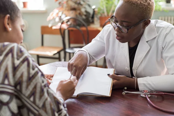 Hispanic patient signs treatment agreement with African female doctor. Young people of mixed race. The trust of the patient and the doctor. Voluntary Informed Consent — 스톡 사진