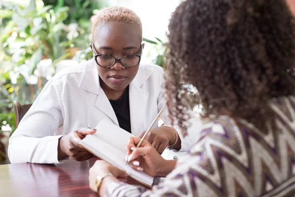 Ισπανόφωνος ασθενής υπογράφει συμφωνία θεραπείας με Αφρικανή γιατρό. Νέοι της μικτής φυλής. Την εμπιστοσύνη του ασθενούς και του γιατρού. Εθελοντική ενημέρωση συναίνεσης — Φωτογραφία Αρχείου