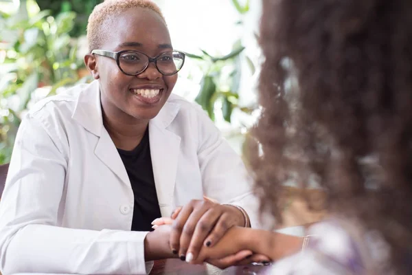 Усміхаючись, африканська дівчинка - лікар потискає руки латиноамериканській жінці - пацієнтці. Довірливість лікаря і пацієнта. Добровільна поінформована згода на лікування. Змішана расова юність у кабінеті лікаря. — стокове фото