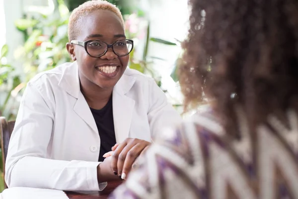Молода афроамериканська жінка-лікар з окулярами потискає руку пацієнту як знак довіри лікаря. Люди змішаної раси У лікарях — стокове фото