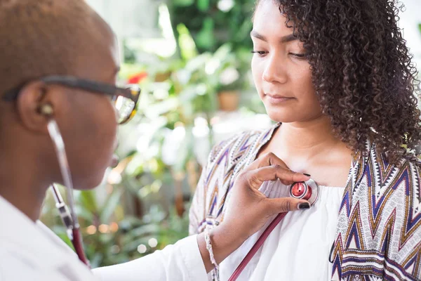Afro-Amerikalı bir doktor, bir hastaya göz kulak olmak için steteskop kullanıyor. Karışık Irk Gençliği