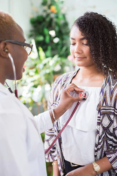 Афроамериканська дівчинка-лікар використовує стетоскоп для проведення аускультації для пацієнта. Змішана расова молодь — стокове фото