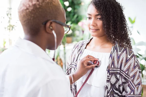 Afro-Amerikalı bir doktor, bir hastaya göz kulak olmak için steteskop kullanıyor. Karışık Irk Gençliği