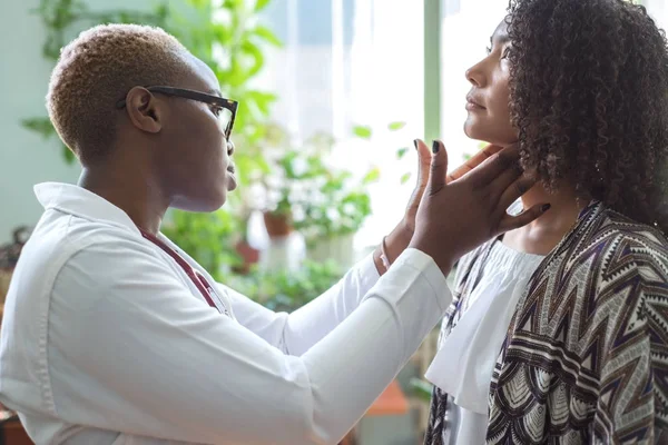 Afro-Amerikalı bir kadın doktor parmaklarıyla muayene ediyor, boynunu ve lenf bezlerini sarıyor. Boyun ağrısı. Karışık ırk doktoru ve hastası.