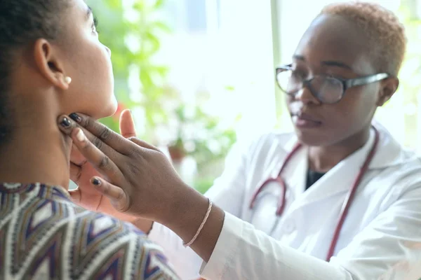 Afrikalı kadın doktor boğazı ağrıyan hastayı izliyor.