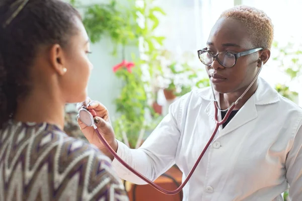 Afro-Amerikalı bir doktor, bir hastaya göz kulak olmak için steteskop kullanıyor. Karışık Irk Gençliği