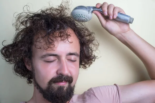 Ritratto di un ragazzo con gli occhi chiusi, cuoio capelluto problematico e capelli lunghi sporchi. Tiene in mano un soffione doccia, diffusore — Foto Stock