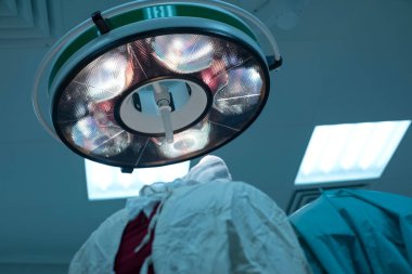 low angle, pediatric surgeons perform surgery in a sterile operating room. The view from the back. Illuminates the operating field lamp