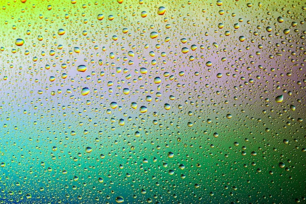 Nahaufnahme von Wassertropfen auf einem Glas. Regenbogen Hintergrund, bunte abstrakte Muster. — Stockfoto