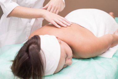 Masör bir kızın elleri, kaplıca salonunda genç bir kadına sırt masajı yapıyor.