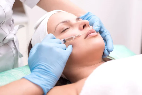 Injektion in die Gesichtshaut einer jungen Frau, aus nächster Nähe. Ein Kosmetiker mit einer Spritze mit einer Nadel führt ein Mittel ein, um Falten im Gesicht im Lippenbereich zu entfernen. — Stockfoto