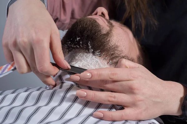 Primo piano della mano di un professionista della barba. tagliare una barba per un giovane con un rasoio pericoloso — Foto Stock