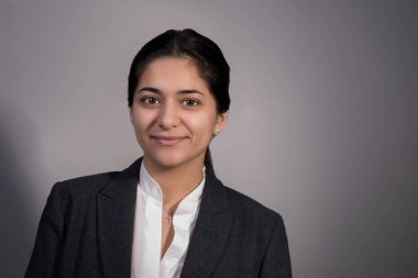 Otuz güzel iş kadını portresi, iş elbisesi içinde, kollarını göğsünde kavuşturmuş, gülümsüyor. Gri arka planda, stüdyo fotoğrafçılığı. İş konsepti