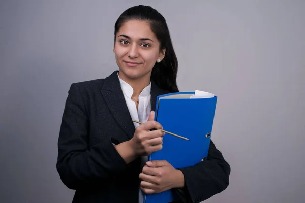 Retrato de uma bela indiana jovem mulher de negócios em um terno de negócios, segurando uma pasta azul com documentos em sua mão, olhando atenciosamente, Fotografia de estúdio de espaço livre — Fotografia de Stock