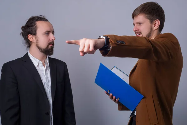 Портрет двох молодих бізнесменів. Бос, тримаючи папку з документами в руці, показує з рукою в бік, з розлюченим обличчям кричить на підлеглих — стокове фото
