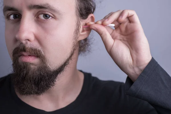 若い髭の男の肖像画だ綿棒を使って耳の中の硫黄をきれいにする男のクローズアップ。耳の健康、ケアとクリーニング — ストック写真