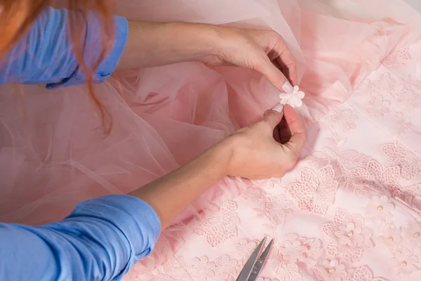 Vue de dessus d'un lieu de travail de couturier dans son atelier de fabrication de vêtements. Vêtements faits main, coud professionnellement des fleurs décoratives sur une robe rose . — Photo