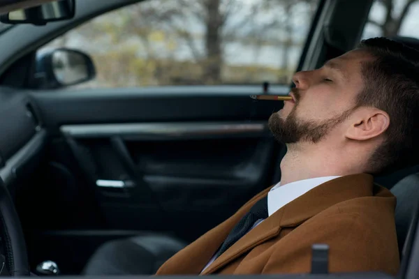 Retrato de un joven borracho durmiendo con un cigarrillo mientras conducía un coche. Primer plano. En un tono cálido y creativo —  Fotos de Stock