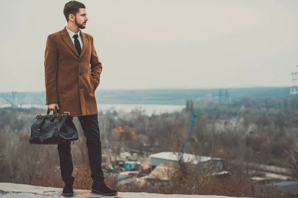 Retrato de un hombre barbudo de treinta años, de estilo empresarial, con una bolsa de cuero en las manos. Contra el cielo, estilo callejero. Concepto de negocio. En teñido creativo . —  Fotos de Stock