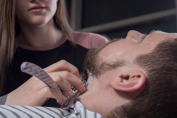 Närbild av handen på en skäggvårdspersonal. skära skägg för en ung man med en farlig rakkniv — Stockfoto
