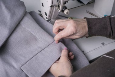 Usta modacı, bir dikiş makinesinin arka planına karşı, yüksek kaliteli kumaştan elbiseler dikiyor, kıyafet üretiminde usta bir profesyonel tarafından el yapımı.
