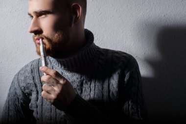 Yakın plan. Modern yüksek teknolojili elektronik sigara içen sakallı genç bir adamın sanat portresi.
