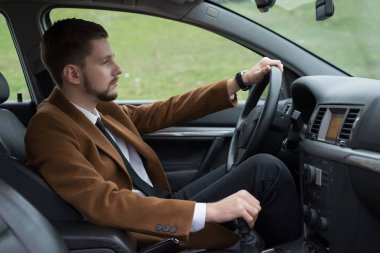 Takım elbiseli, araba kullanan sakallı bir gencin portresi.