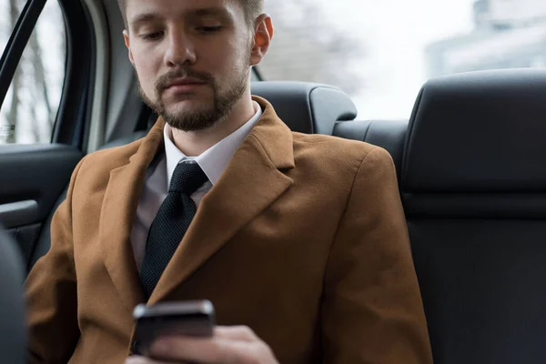 Retrato de un joven de treinta años. Empresario en un estilo de negocio de la ropa. Viaja en el asiento del pasajero en la oficina para trabajar, resolver problemas en el teléfono inteligente, hablar por teléfono —  Fotos de Stock