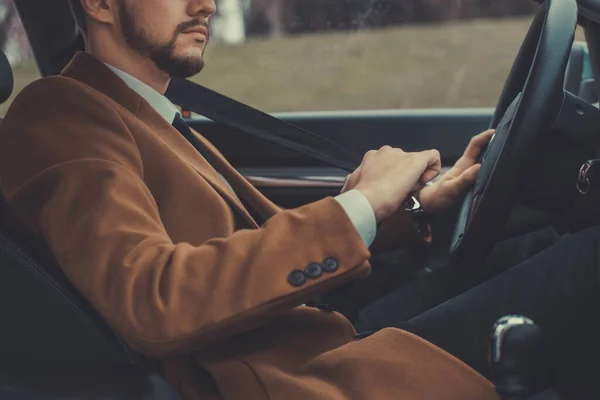 Primer plano retrato de un tipo barbudo en un traje de negocios, se abrocha el cinturón de seguridad, sentado al volante de un coche —  Fotos de Stock